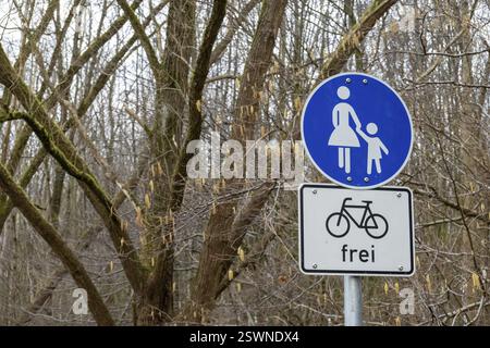 Panneau rond bleu de chemin partagé pour les piétons avec un adulte et un enfant, et un panneau rectangulaire pour les vélos ci-dessous, dans une forêt Banque D'Images