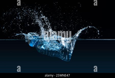 Vue avant d'une bouteille en plastique transparent immergée dans l'eau causant une éclaboussure sur un fond noir Banque D'Images