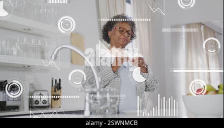 Image du traitement des données sur une femme afro-américaine senior buvant du café dans la cuisine Banque D'Images