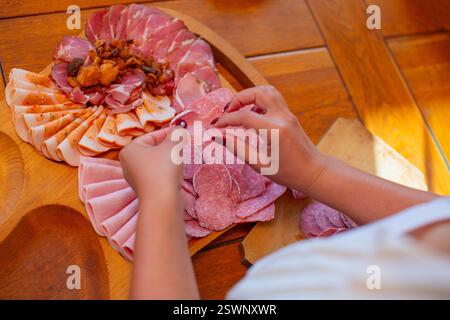Mains disposer les tranches de viande sur une planche de charcuterie en bois pendant la préparation des aliments. Banque D'Images