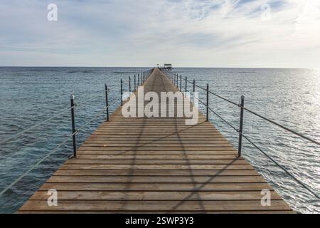 Jetée en bois s'étendant dans la mer calme vers une structure lointaine, créant une scène sereine et accueillante à marsa alam, en égypte Banque D'Images