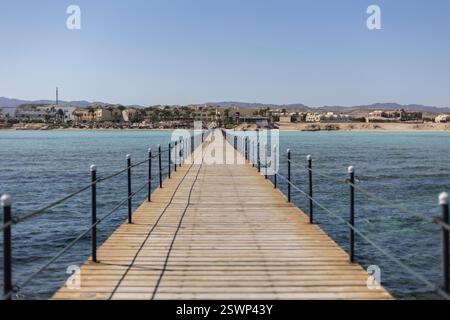 Jetée en bois s'étendant dans l'eau turquoise claire, menant à une station balnéaire à marsa alam, en égypte, par une journée ensoleillée Banque D'Images