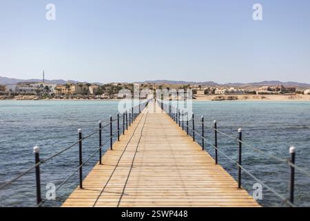 Jetée en bois s'étendant dans l'eau turquoise calme, menant à une station balnéaire à marsa alam, en égypte, offrant une vue sereine sur la côte Banque D'Images