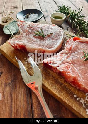 Steaks de porc cru sur l'os et herbes sur une planche à découper en bois. Viande de porc fraîche. Directement au-dessus. Banque D'Images