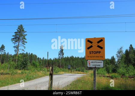 Värmland, Suède. 20 juillet 2021. Panneaux et symboles de passage à niveau. Route en gravier avec nature verte sur les côtés. Lignes électriques dans l'air pour les trains Banque D'Images