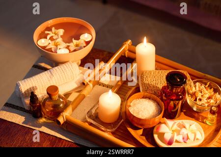 Plan à angle élevé de plateau en bois avec des produits cosmétiques, des bougies d'arôme et des fleurs séchées sur la table basse Banque D'Images