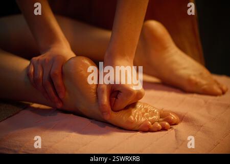 Gros plan moyen des mains masseuses professionnelles massant les pieds féminins avec de l'huile chauffante Banque D'Images