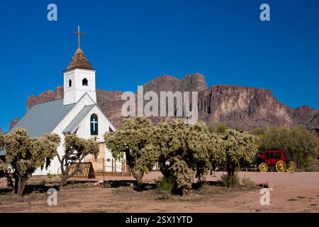 Petite église blanche avec une croix sur le dessus se trouve en face d'une grande montagne. L'église est entourée d'arbres et un chariot est garé devant elle. T Banque D'Images