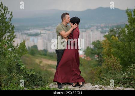 Heureux couple musulman aimant mari embrassant sur le front de la femme dans le hijab à l'extérieur de wit paysage urbain sur le fond. Banque D'Images