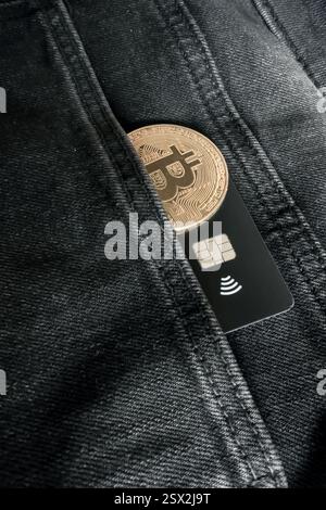 Carte de crédit à côté d'une pièce physique Bitcoin à l'intérieur d'une poche de Jean noir Banque D'Images
