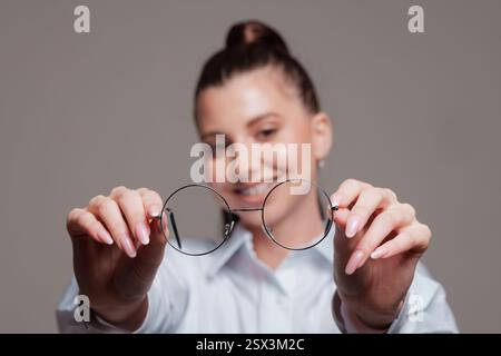 Femme souriante tenant des lunettes rondes devant elle, offrant un concept de vision claire, gros plan. Banque D'Images