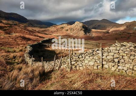Un mur de pierres sèches ensoleillé serpente au loin sur les puits Coniston dans l'est du parc national Lake District vers les montagnes en hiver. Banque D'Images