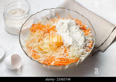 Un bol en verre rempli de chou blanc râpé et de carottes râpées, avec de l'œuf cru et de la farine pour une recette de pancakes aux légumes faits maison ou de fritter Banque D'Images