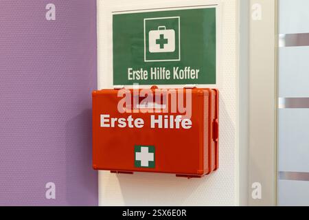 Une trousse de premiers soins rouge vif est solidement fixée sur un mur, accompagnée d'un panneau vert de santé et de sécurité indiquant qu'une aide d'urgence est disponible, ensuri Banque D'Images
