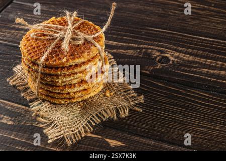Une pile de gaufres au caramel fraîchement préparées nouées avec de la ficelle repose sur un tapis rustique en toile de jute, parfait pour célébrer la journée nationale du caramel. Le col doré chaud Banque D'Images