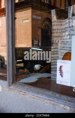 Cremona, Italie 9 février 2025 Luthier restaure soigneusement un violon dans son atelier, vu de l'extérieur par une fenêtre Banque D'Images