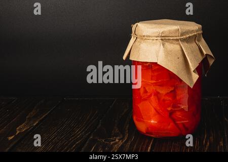 Les tomates marinées rouge vif sont stockées dans un bocal en verre, scellé avec une couverture en papier. Cette conservation maison reflète une tradition locale d'utilisation du saindoux Banque D'Images