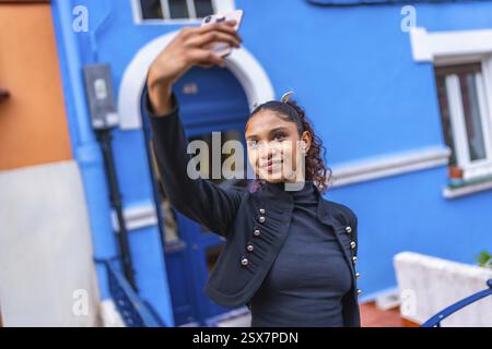 Beauté jeune femme afro américaine prenant selfie à l'extérieur d'une maison colorée bleue dans la ville Banque D'Images