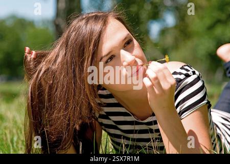 Une jeune femme allongée sur un pré de fleurs avec une tige de fleur dans son esprit Banque D'Images