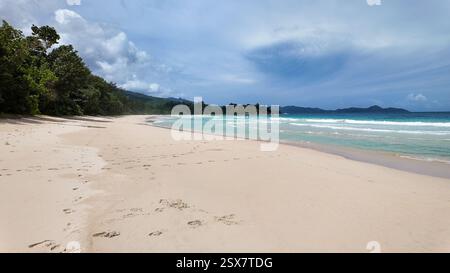 Une plage tropicale pittoresque qui s'étend le long de la côte, bordée par des eaux turquoises et une végétation luxuriante. Grand Anse. Seychelles, Mahé. Banque D'Images
