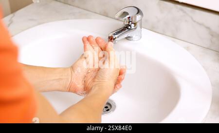 Homme se lavant les mains avec du savon et de l'eau dans le lavabo de la salle de bains Banque D'Images