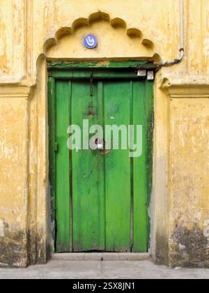 Porte verte altérée avec arc festonné et signe numérique bengali dans le vieux Dhaka, reflétant l'influence moghole et le patrimoine architectural local. Banque D'Images