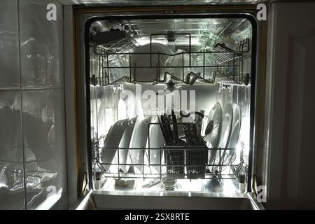 Détail de l'intérieur d'un lave-vaisselle en acier inoxydable intégré dans une armoire de cuisine blanche à côté d'un mur avec des carreaux réfléchissants avec deux barreaux métalliques Banque D'Images