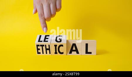 Symbole éthique et juridique. La main d'homme d'affaires pointe sur des cubes en bois tournés avec des mots éthiques et légaux. Beau fond jaune. Affaires et éthique Banque D'Images
