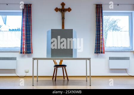 Inkofen, Allemagne. 23 février 2025. Un bureau de vote vide se tient sur une table avec une croix en bois accrochée au mur devant. Les élections anticipées pour le 21e Bundestag allemand auront lieu dimanche. Crédit : Armin Weigel/dpa/Alamy Live News Banque D'Images