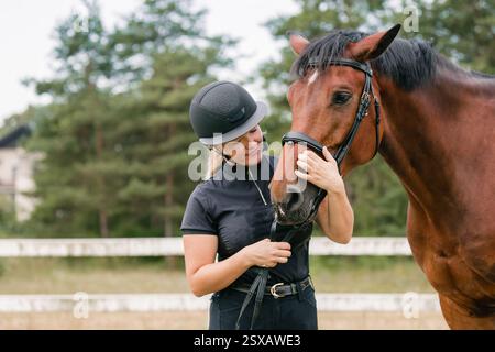 Femme avec un casque noir qui a une belle tête de cheval châtaignier, gros plan. Concept de relation humaine et animale. Banque D'Images