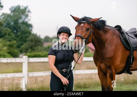 Une cycliste féminine en vêtements équestres tenant les rênes et conduisant son beau cheval de châtaignier à selles. Concept d'activité d'équitation. Banque D'Images