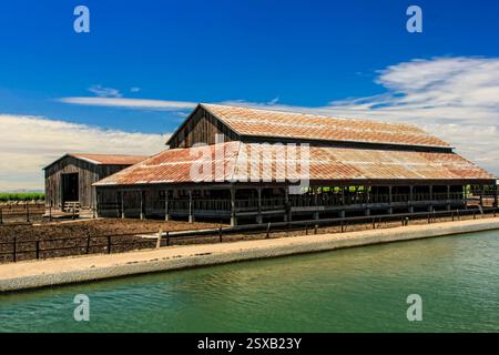 Grange avec un toit rouge et une clôture verte. La grange est à côté d'un plan d'eau Banque D'Images