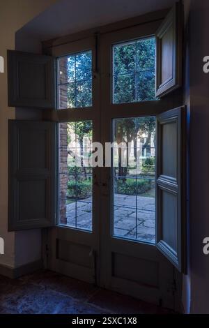 Vieille double porte en bois avec verre et panneaux menant au patio avec arbres et plantes dans le Parador de Turismo, ville d'Almagro, Ciudad Real, Espagne Banque D'Images