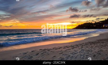 Coucher de soleil doré sur l'océan avec des vagues se jetant sur la rive sablonneuse, reflétant les couleurs chaudes du ciel. Seychelles, Mahé. Banque D'Images