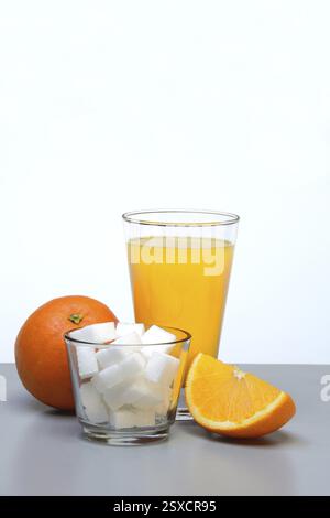 Jus d'orange dans un verre à boire, une demi-orange et des cubes de sucre Banque D'Images