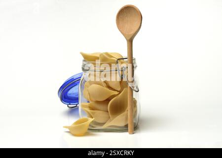 Conchiglione dans un pot en verre avec cuillère de cuisson, variété de pâtes italiennes Banque D'Images