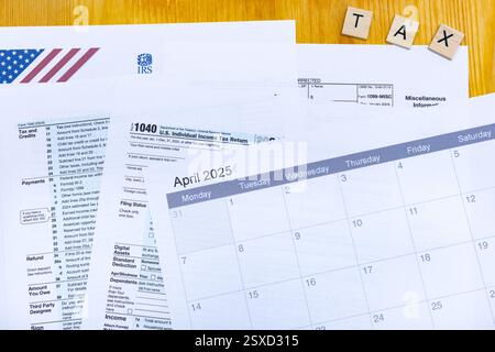 Une collection de documents fiscaux américains, y compris les formulaires IRS 1040 et 1099-MISC, est étalée sur un bureau en bois. Un calendrier affichant le 2025 avril est promine Banque D'Images