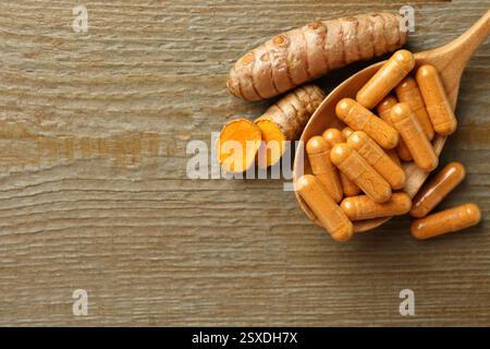 Capsules de curcuma en cuillère et racines sur table en bois, pose à plat. Espace pour le texte Banque D'Images