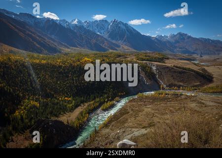 Une superbe rivière de montagne coule à travers une forêt, entourée de sommets enneigés et de vallées Banque D'Images