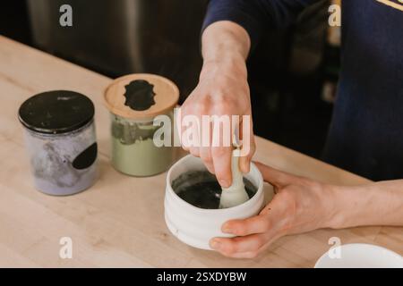 Mains fouettant le matcha dans un bol en céramique sur un comptoir de café en bois Banque D'Images