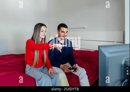 Jeune couple jouant à des jeux vidéo dans la chambre à coucher à l'aide d'une manette sans fil Banque D'Images