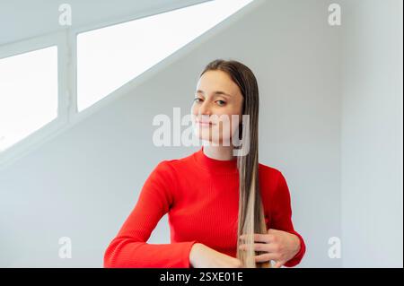 Jeune femme peignant ses longs cheveux avec un peigne, portant un pull rouge Banque D'Images