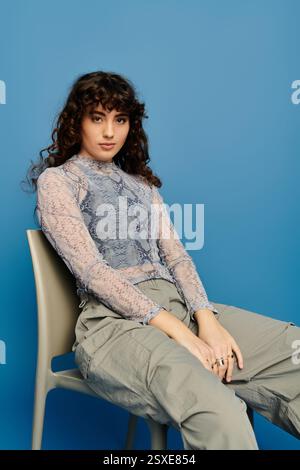 Femme élégante avec les cheveux bouclés exprime des émotions tout en étant assise sur un fond bleu vif. Banque D'Images