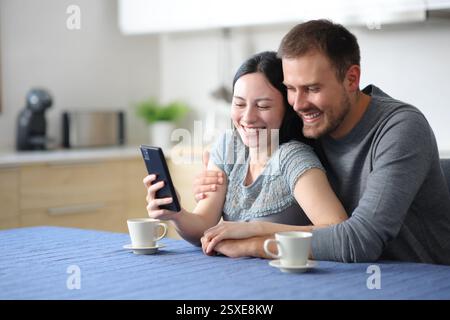 Heureux couple interracial dans l'amour vérifier le téléphone dans la cuisine à la maison Banque D'Images