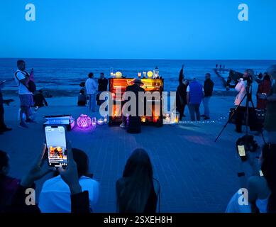 Odessa, Ukraine, 25 mai 2024 : pianiste jouant du piano avec contre-jour sur le bord de mer et beaucoup de gens l'écoutant la nuit d'été. Concert de musicien homme jouant du piano avec des spectateurs à l'extérieur en soirée Banque D'Images