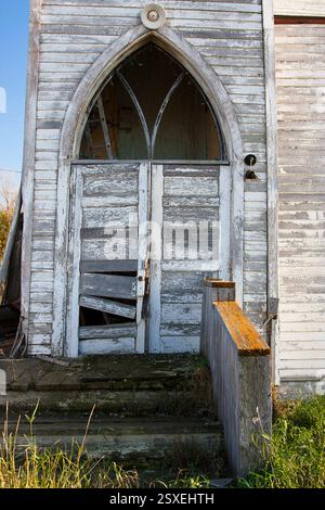 La porte d'entrée d'un bâtiment est ouverte et a une serrure cassée. La porte est blanche et a un cadre en bois. Le bâtiment est vieux et a beaucoup de caractère Banque D'Images