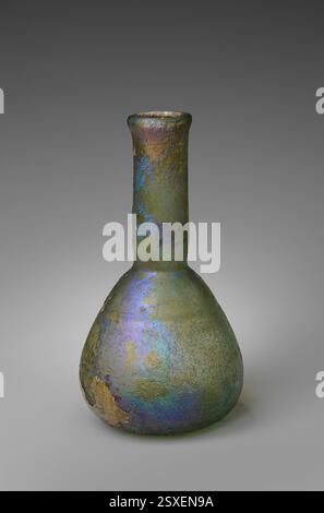 Ce flacon de parfum en verre romain, datant du 1er au 2ème siècle de notre ère, présente un corps translucide bleu-vert pâle et se caractérise par un bord évasé et un corps ovoïde accroupi. La bouteille montre des signes d'altération profonde et d'iridescence brillante, typique des artefacts de verre anciens. Banque D'Images