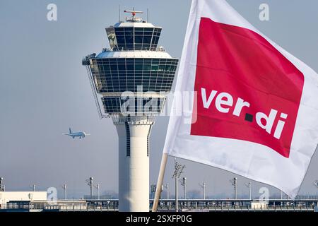 Munich, Bavière, Allemagne - 24 février 2025 : PHOTOMONTAGE, image symbolique avec un drapeau Verdi devant la tour et un avion à l'aéroport de Munich. Symbole pour grève annoncée ou grève d'avertissement et perturbation de la circulation aérienne et des passagers. *** FOTOMONTAGE, Symbolbild mit einer Verdi Fahne vor dem Tower und einem Flugzeug am Münchner Flughafen. Symbole für angekündigten Streik bzw. Warnstreik und Beeinträchtigungen des Flugverkehrs und der Passagiere. Banque D'Images