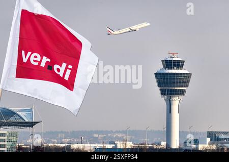 Munich, Bavière, Allemagne - 24 février 2025 : PHOTOMONTAGE, image symbolique avec un drapeau Verdi devant la tour et un avion à l'aéroport de Munich. Symbole pour grève annoncée ou grève d'avertissement et perturbation de la circulation aérienne et des passagers. *** FOTOMONTAGE, Symbolbild mit einer Verdi Fahne vor dem Tower und einem Flugzeug am Münchner Flughafen. Symbole für angekündigten Streik bzw. Warnstreik und Beeinträchtigungen des Flugverkehrs und der Passagiere. Banque D'Images