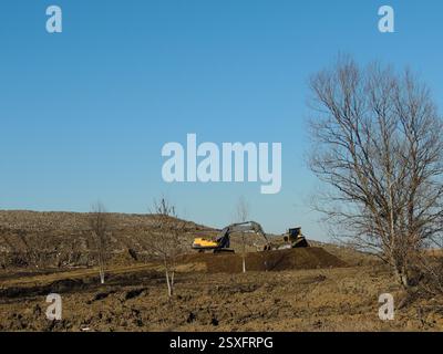équipement de construction travaillant sur une colline avec de la terre, un bulldozer et une pelle hydraulique nivelant une zone de terre sur une colline, machines en marche Banque D'Images
